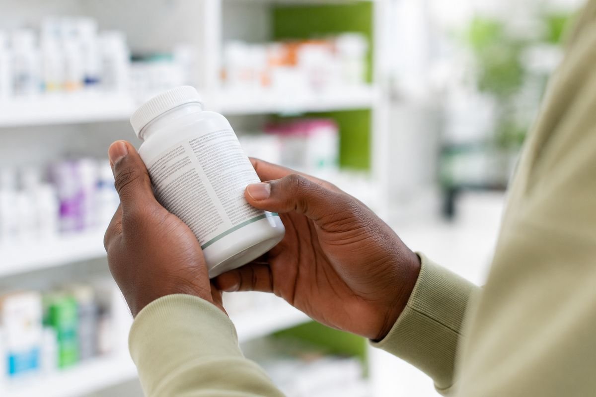Personne tenant un flacon de complément alimentaire et lisant attentivement son étiquette devant les rayons d'une pharmacie